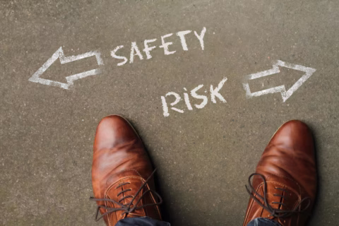 A person wearing brown leather shoes stands on pavement with chalk arrows pointing left to Safety evaluation and right to Risk. - KindestMind