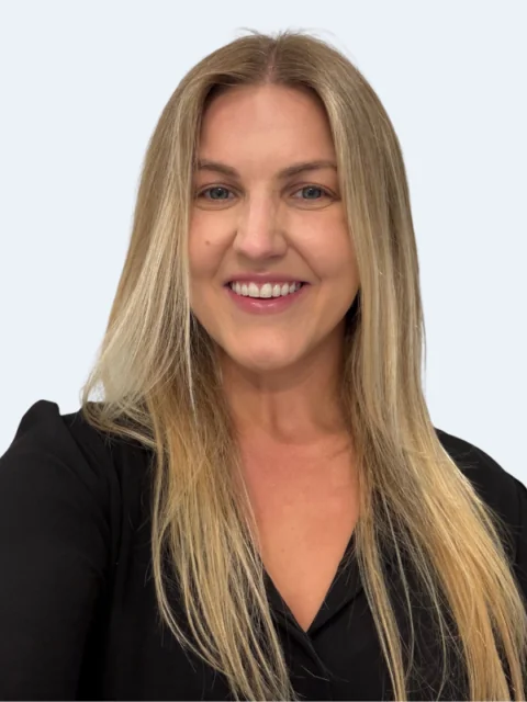 A woman with long, straight blonde hair and a black top is smiling at the camera against a plain, light background, representing the Clinical Team. - KindestMind